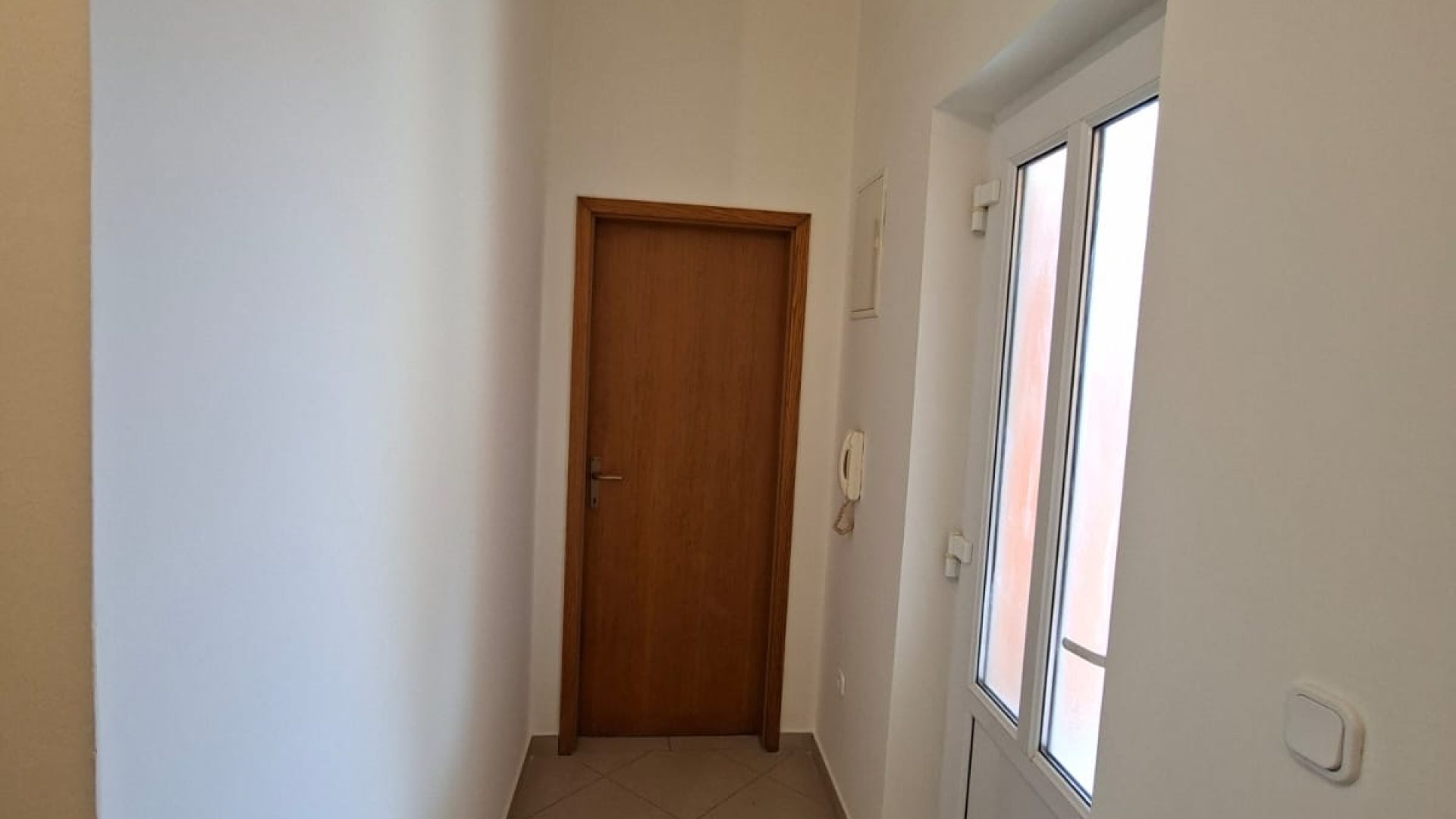 Uži hodnik s drvenim vratima i staklenim izlaznim vratima u potkrovnom stanu.