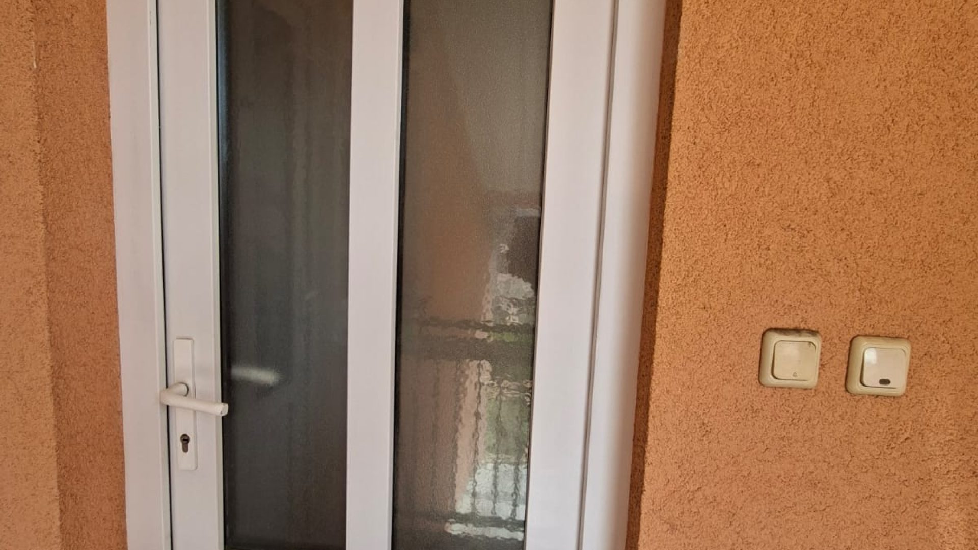 Bijela ulazna vrata s mat staklom i narančastim zidom.