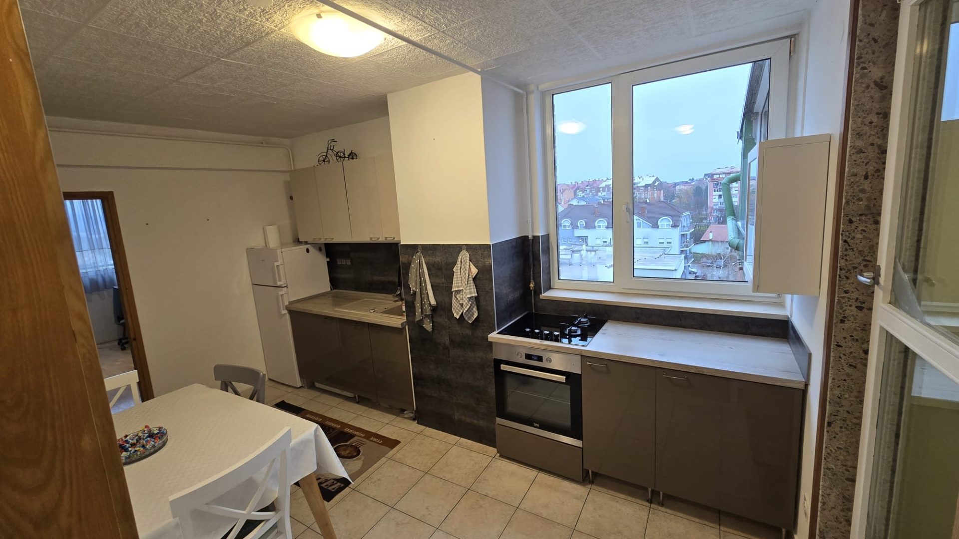 Kuhinja s blagovaonskim stolom, velikim prozorima i modernim kuhinjskim elementima.