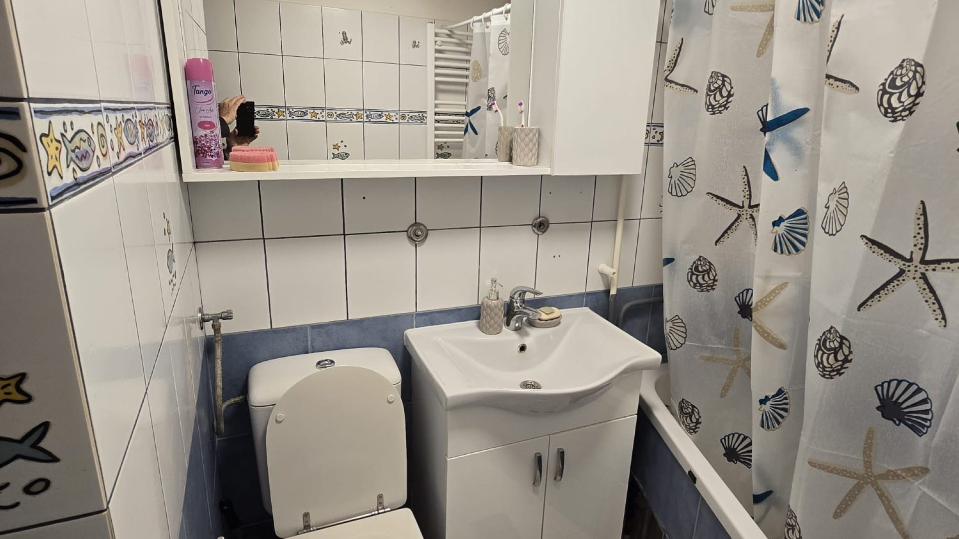 Kupaonica s kadom, umivaonikom, WC-om i morskim dekorom na pločicama i zavjesi.