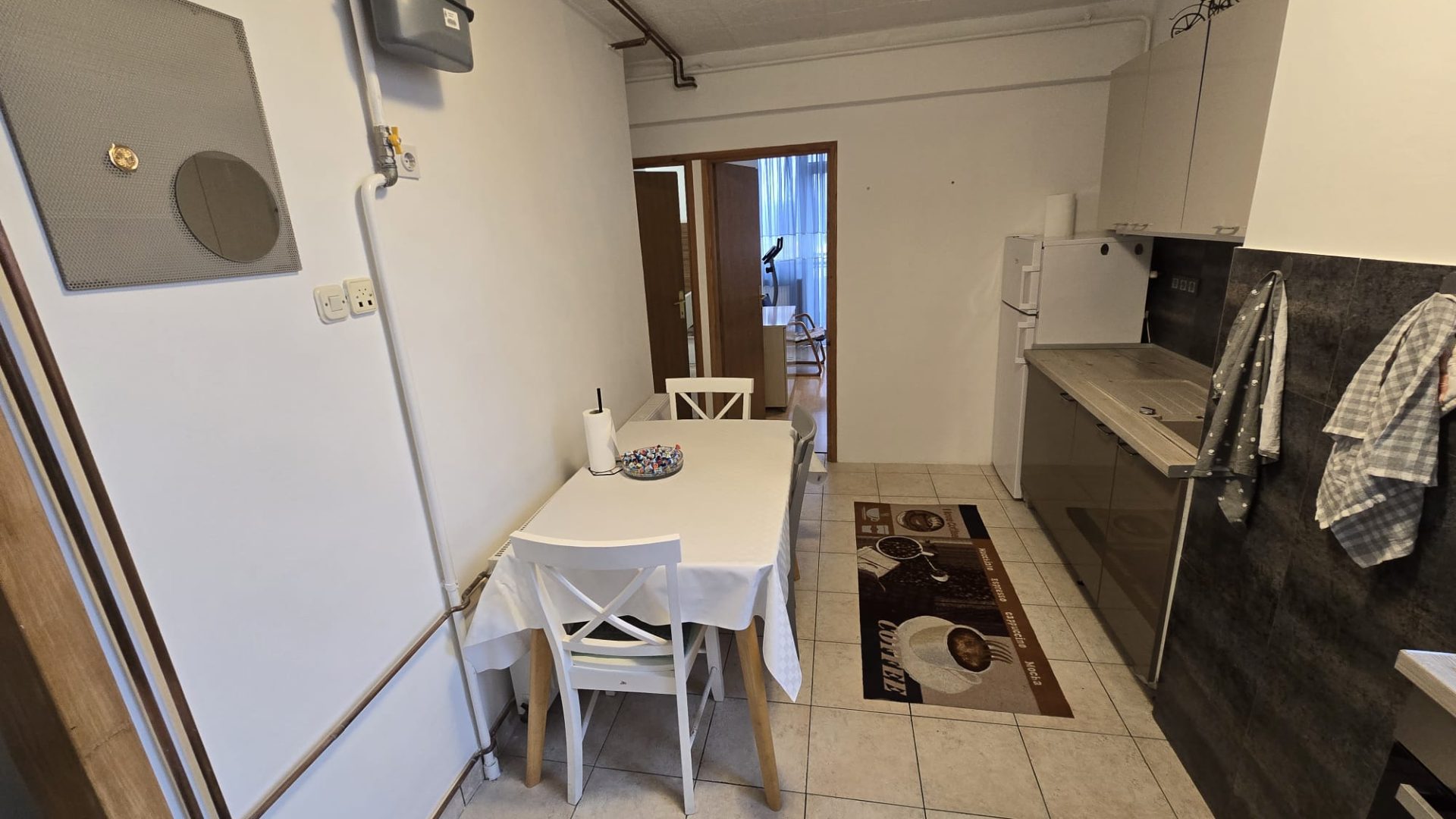 Kuhinja s blagovaonskim stolom, bijelim stolicama i modernim kuhinjskim elementima.