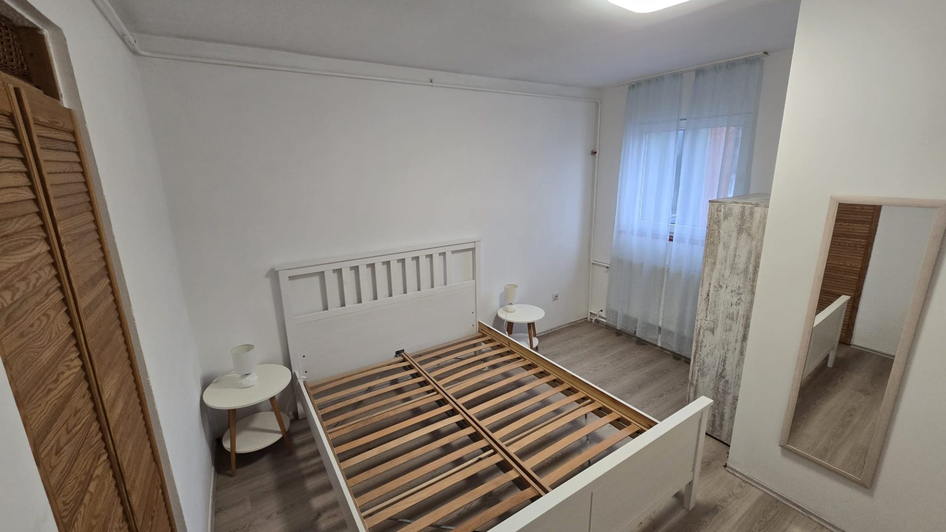 Spavaća soba s bračnim krevetom, noćnim ormarićima i drvenim ormarom.