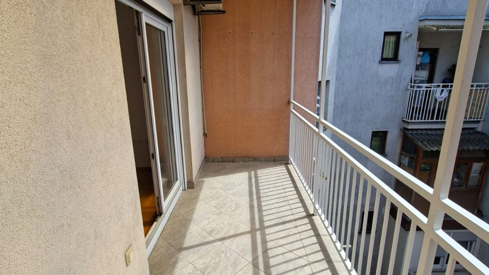 Balkon s pločicama, bijelom ogradom i klima uređajem.