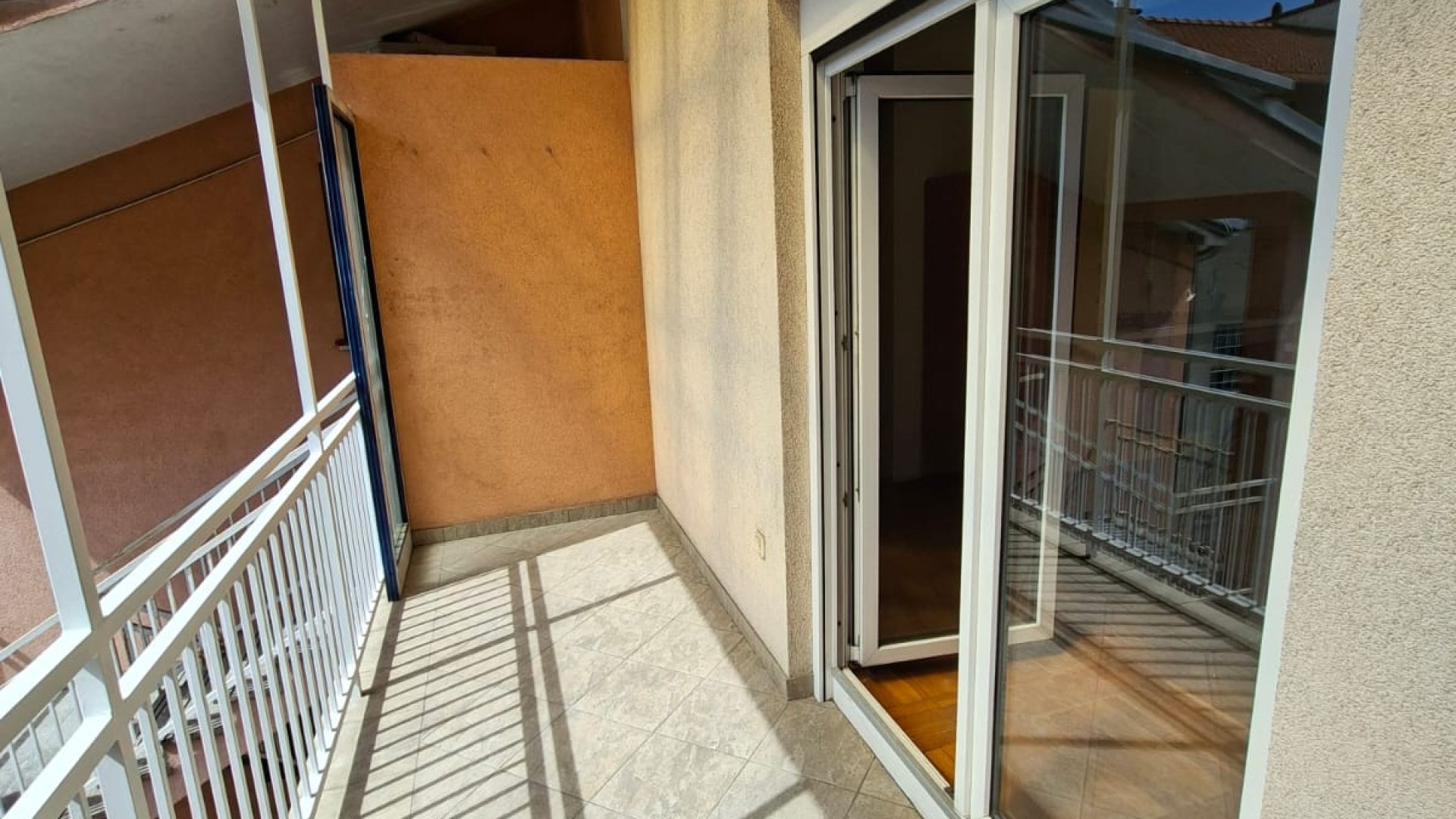 Balkon s bijelom ogradom, nadstrešnicom i kliznim vratima.