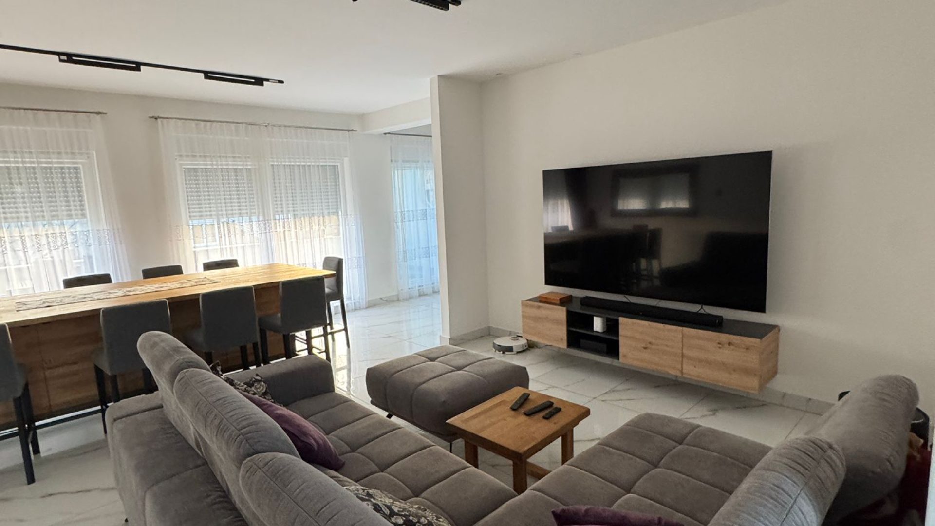Dnevni boravak s TV‑om, sivom garniturom i modernim drvenim elementima.