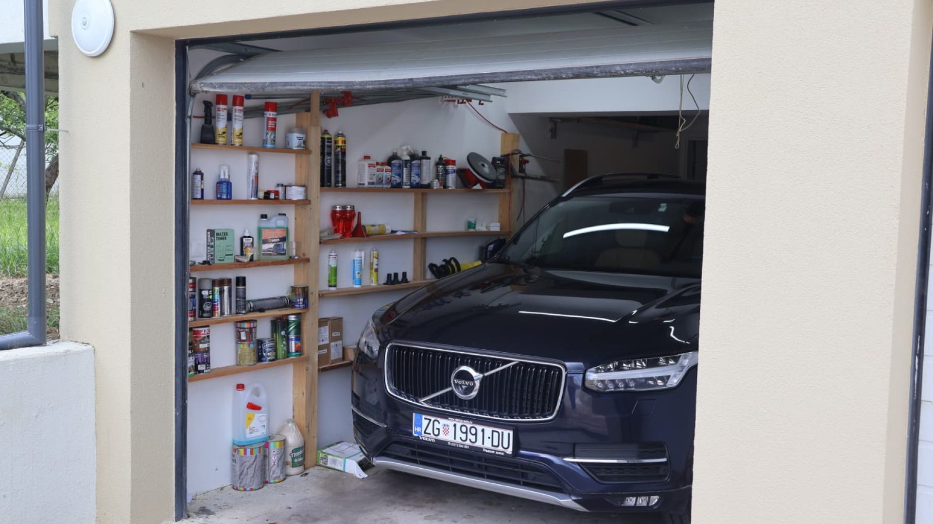 Garaža s parkiranim SUV‑om i policama za alat i opremu.