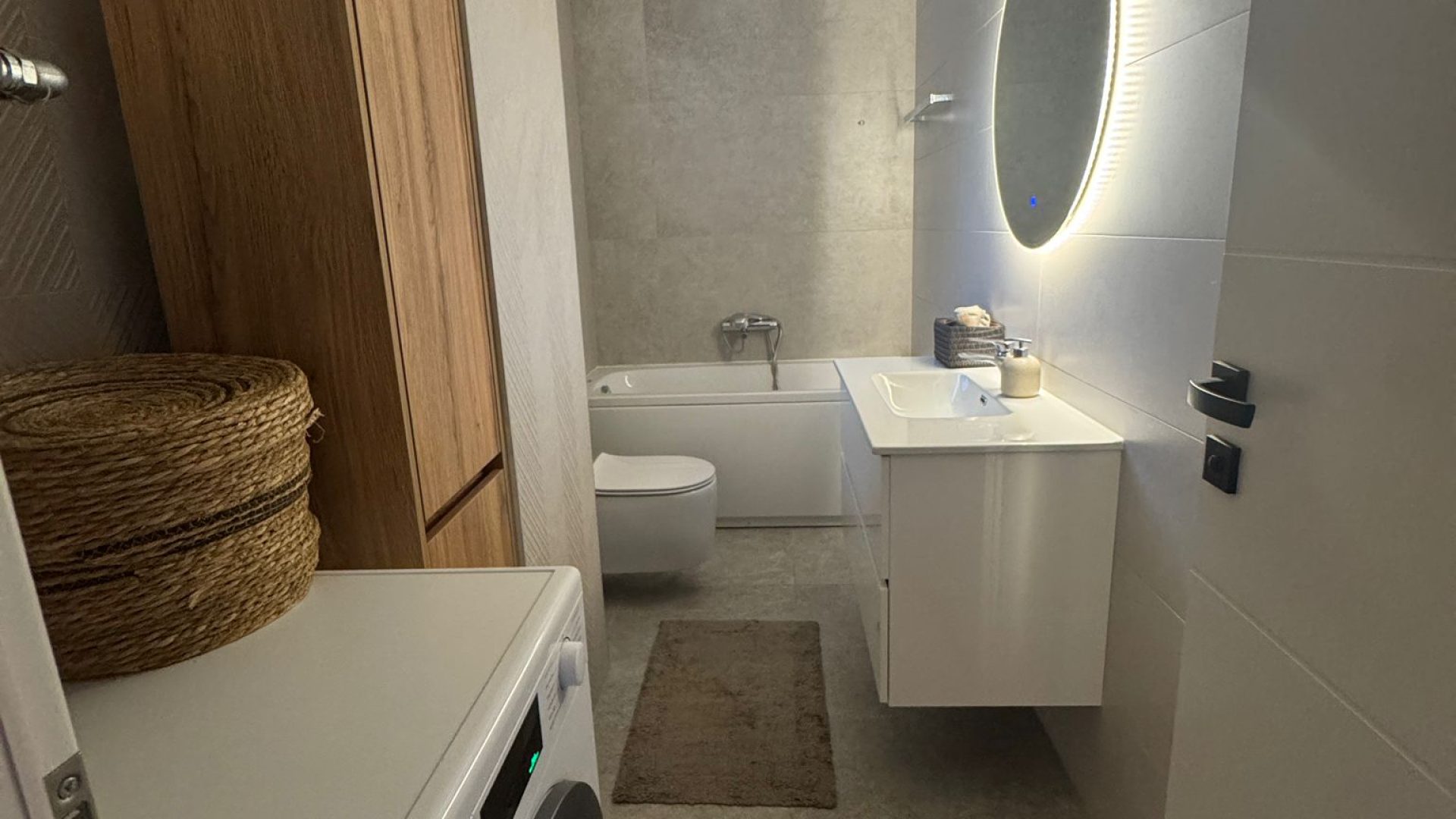 Kupaonica s kadom, visećim ormarićem i modernim sivim pločicama.