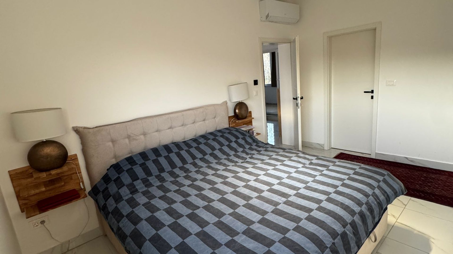 Spavaća soba s velikim krevetom, modernim noćnim ormarićima i bijelim zidovima.